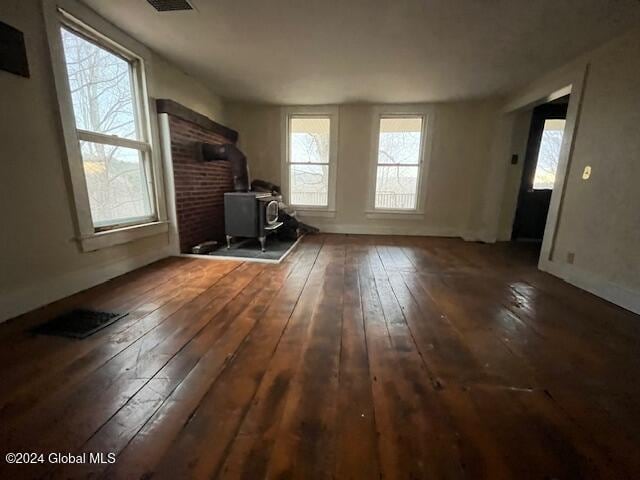 unfurnished living room featuring a wood stove, plenty of natural light, and dark hardwood / wood-style floors