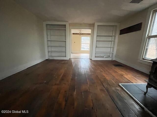 unfurnished living room featuring built in features, dark hardwood / wood-style flooring, and a wood stove