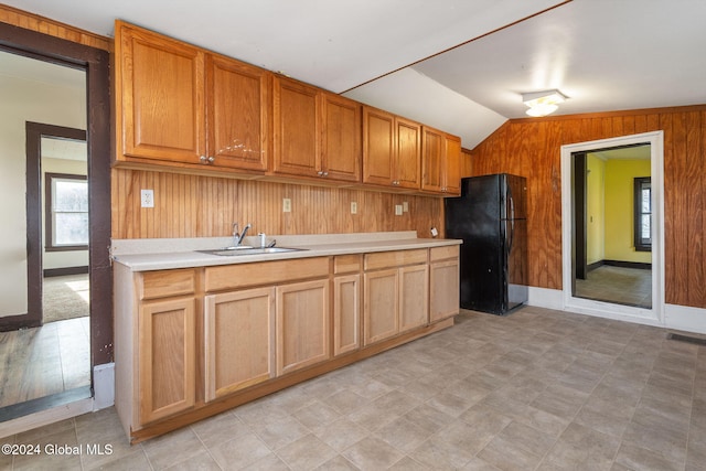 kitchen featuring black refrigerator, vaulted ceiling, wood walls, and sink