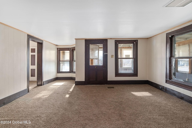 foyer entrance featuring crown molding, carpet, and wood walls