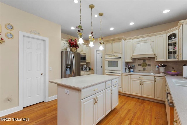 kitchen with light wood-type flooring, premium range hood, stainless steel appliances, a kitchen island, and hanging light fixtures