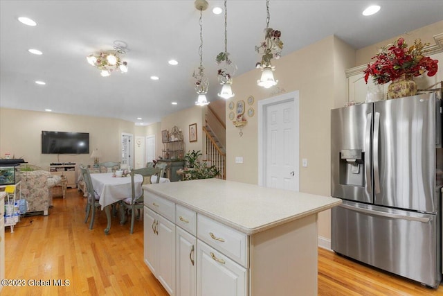 kitchen with pendant lighting, white cabinets, stainless steel fridge, light wood-type flooring, and a kitchen island