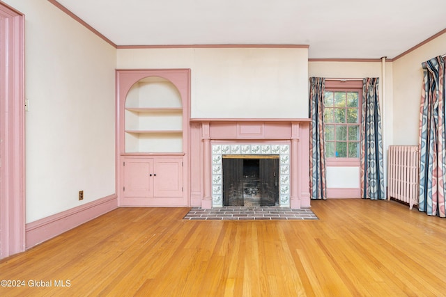 unfurnished living room with light hardwood / wood-style flooring, crown molding, radiator heating unit, and built in shelves