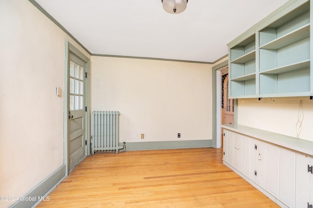 empty room featuring crown molding, radiator heating unit, and light wood-type flooring