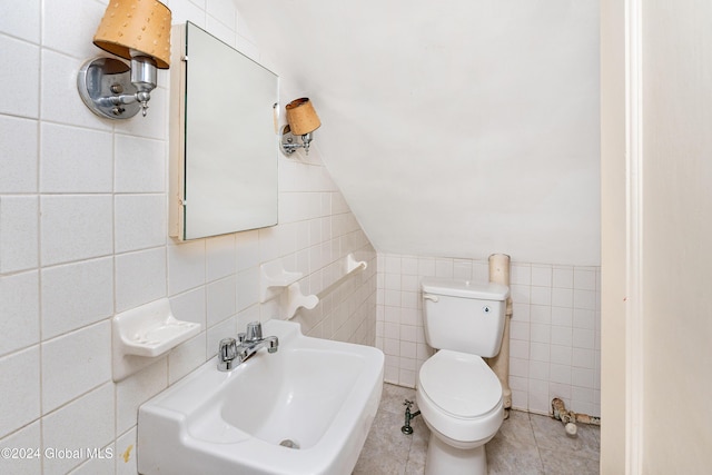 bathroom featuring toilet, sink, vaulted ceiling, tile walls, and tile patterned flooring