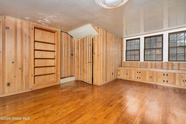 additional living space with vaulted ceiling, built in shelves, hardwood / wood-style floors, and wood walls