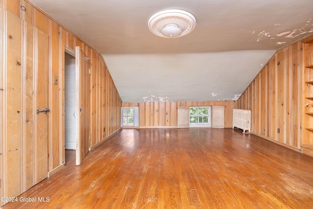 bonus room with hardwood / wood-style flooring, radiator heating unit, wood walls, and vaulted ceiling