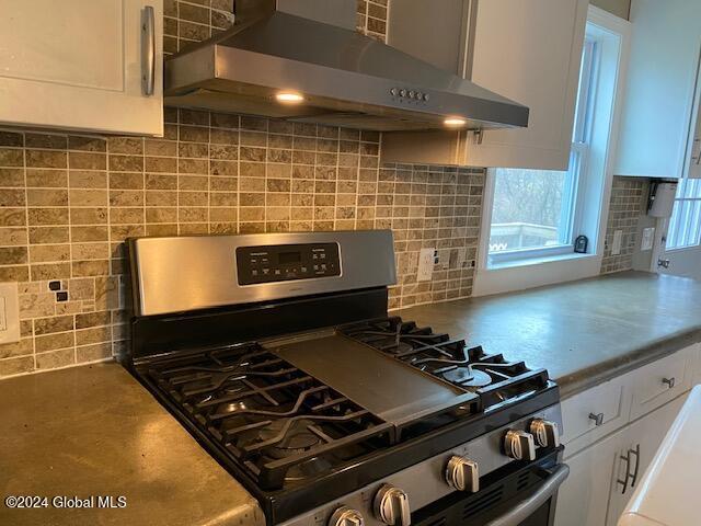 kitchen featuring white cabinets, backsplash, stainless steel range with gas cooktop, and wall chimney range hood