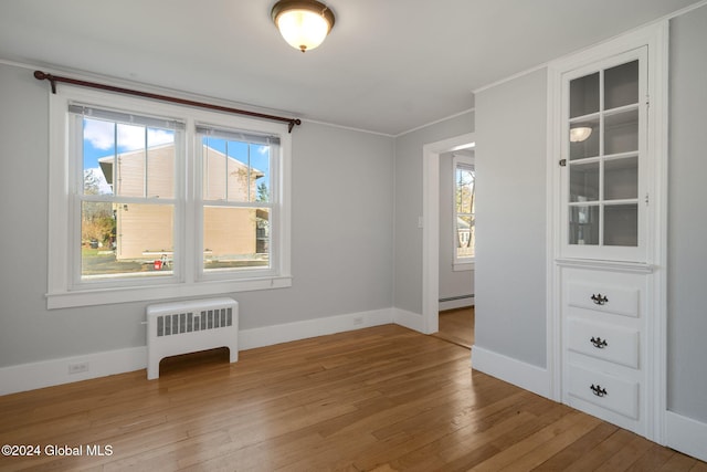 spare room with radiator heating unit, light wood-type flooring, baseboard heating, and a healthy amount of sunlight