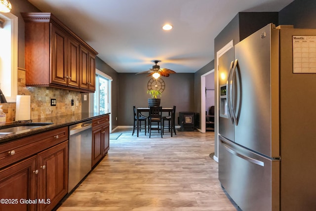 kitchen featuring ceiling fan, light hardwood / wood-style flooring, dark stone counters, decorative backsplash, and appliances with stainless steel finishes