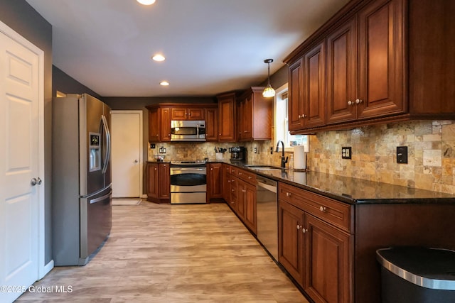 kitchen featuring decorative light fixtures, stainless steel appliances, dark stone countertops, and sink