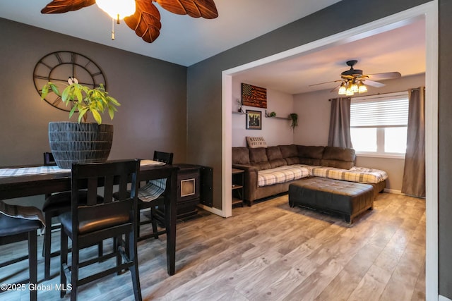 living room featuring a wood stove, ceiling fan, and light hardwood / wood-style flooring