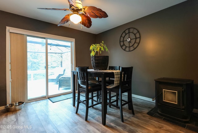 dining area with ceiling fan, wood-type flooring, and a wood stove