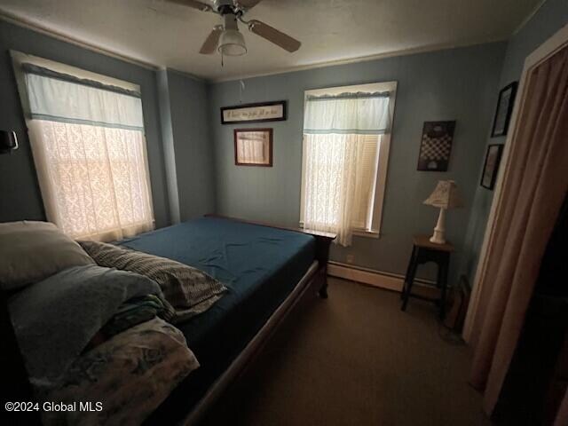 carpeted bedroom with ceiling fan and a baseboard heating unit