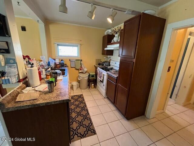 kitchen with dark stone counters, rail lighting, ornamental molding, light tile patterned flooring, and white range oven