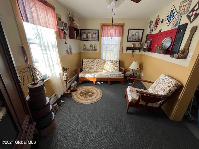 living area with baseboard heating, a wealth of natural light, ceiling fan, and carpet