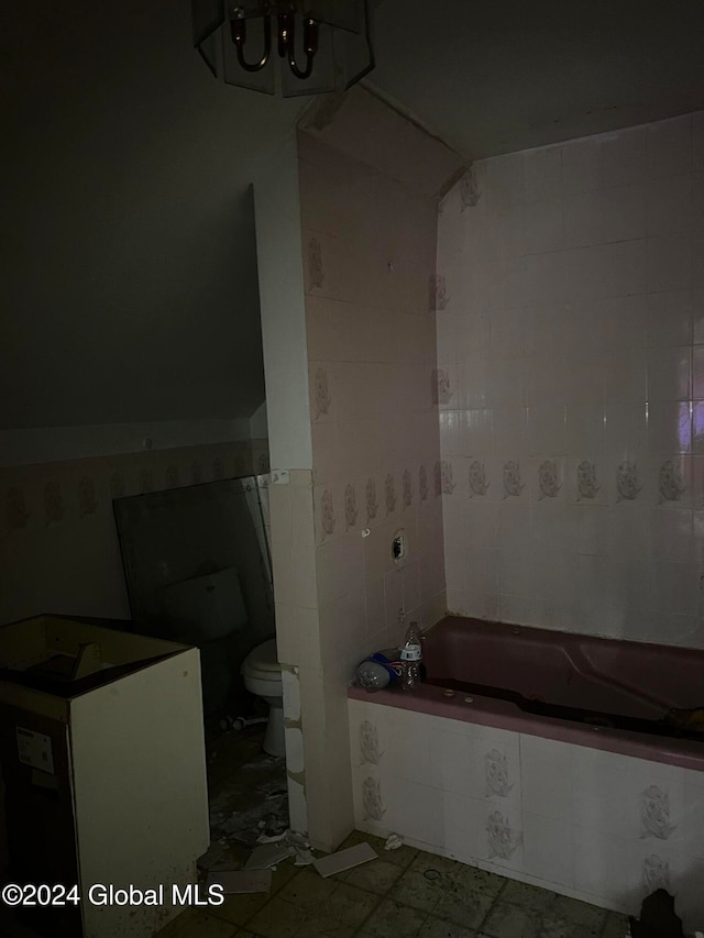 bathroom with a tub to relax in, toilet, and tile walls