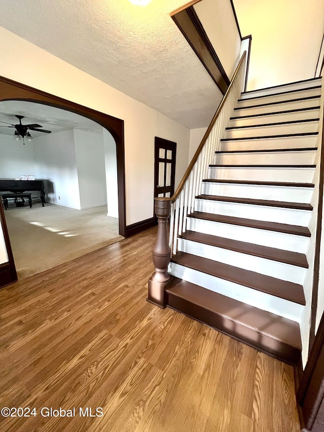 stairs with hardwood / wood-style floors, a textured ceiling, and ceiling fan