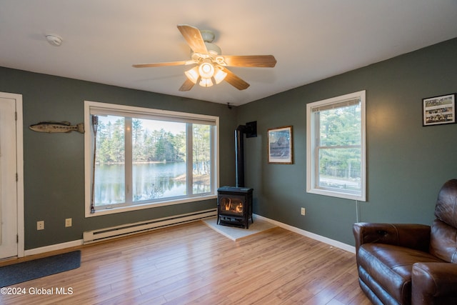 sitting room with a baseboard radiator, plenty of natural light, light hardwood / wood-style flooring, and a wood stove