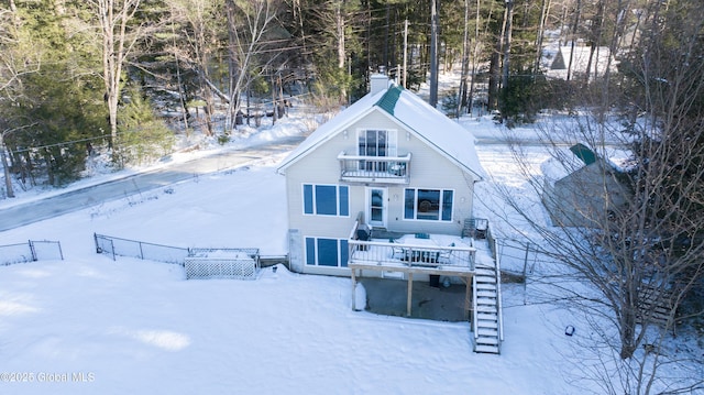 snow covered back of property with a wooden deck and a balcony