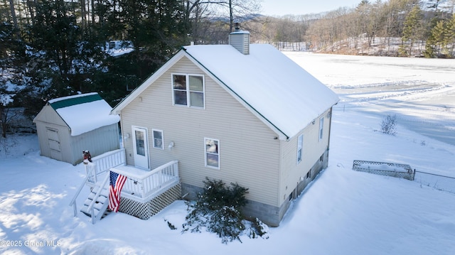 snow covered house featuring a storage unit