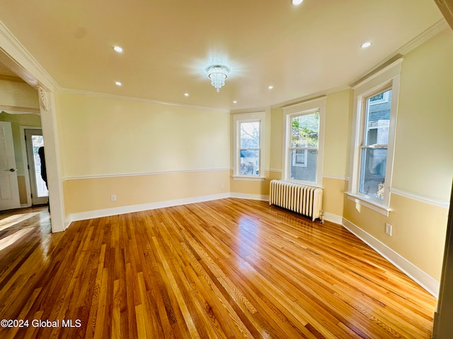 empty room with light hardwood / wood-style floors, radiator heating unit, and ornamental molding