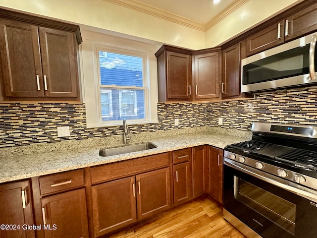 kitchen featuring backsplash, crown molding, sink, light wood-type flooring, and stainless steel appliances