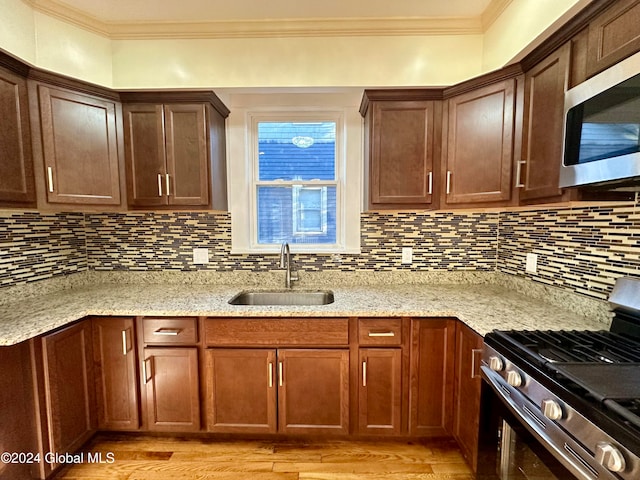 kitchen featuring stainless steel appliances, light stone counters, crown molding, and sink