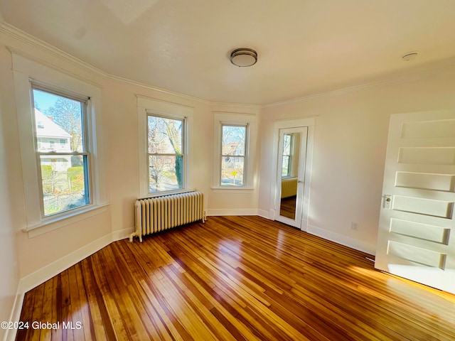 unfurnished room with wood-type flooring, ornamental molding, radiator, and a healthy amount of sunlight