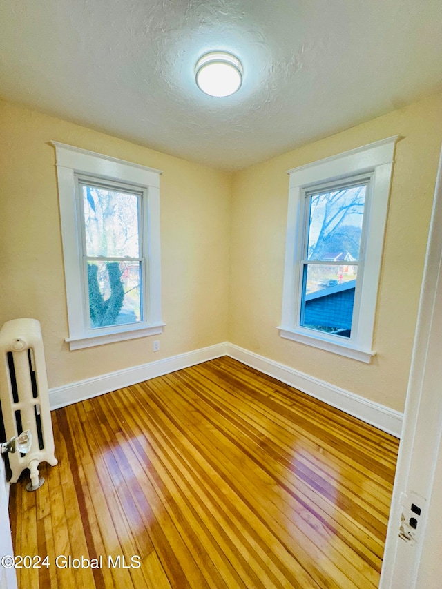 spare room featuring radiator, a healthy amount of sunlight, a textured ceiling, and wood-type flooring