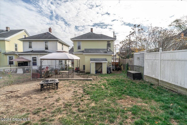 back of house featuring a gazebo, a fire pit, a storage shed, and a lawn