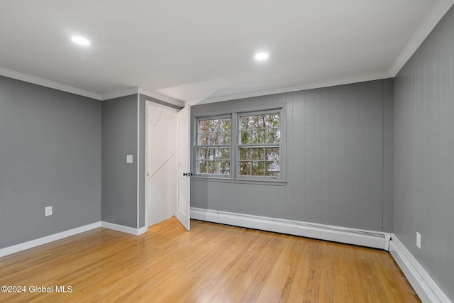 empty room with wooden walls, light hardwood / wood-style floors, crown molding, and a baseboard heating unit