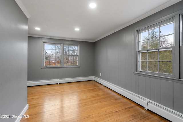 unfurnished room featuring baseboard heating, a wealth of natural light, crown molding, and light wood-type flooring