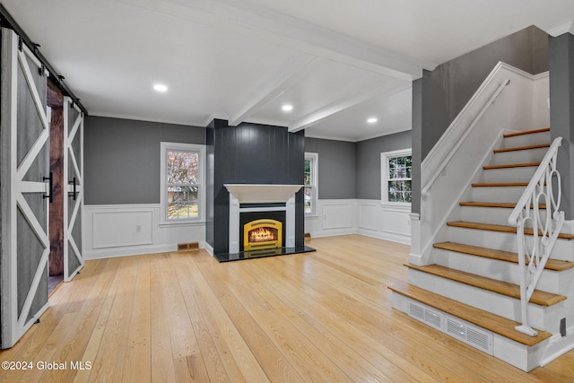 unfurnished living room with hardwood / wood-style floors, a barn door, and beamed ceiling