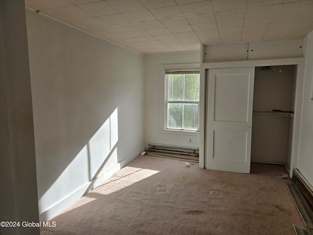 unfurnished bedroom with light carpet, a baseboard radiator, and a closet