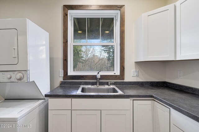 kitchen featuring white cabinets, stacked washer / drying machine, and sink