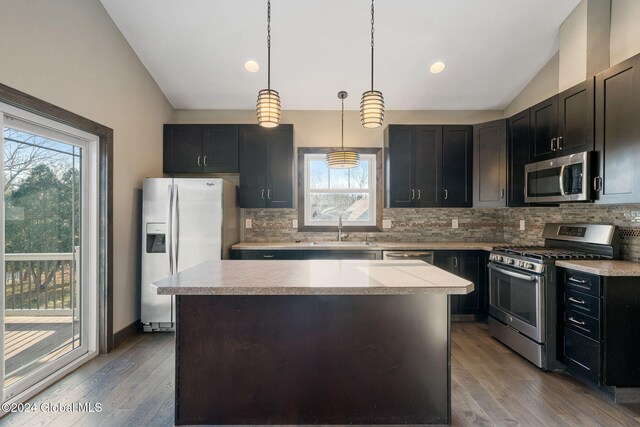 kitchen with appliances with stainless steel finishes, vaulted ceiling, decorative light fixtures, light hardwood / wood-style flooring, and a center island