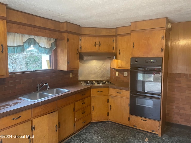 kitchen featuring tasteful backsplash, a textured ceiling, black double oven, stainless steel gas cooktop, and sink