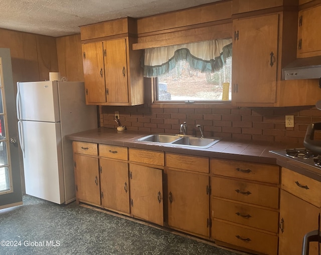 kitchen with white refrigerator, sink, decorative backsplash, a textured ceiling, and tile counters