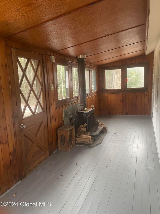 misc room featuring a wood stove, wooden walls, a healthy amount of sunlight, and lofted ceiling