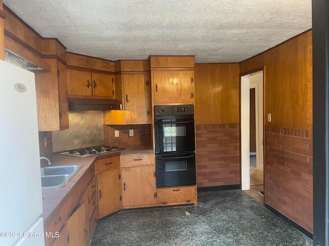 kitchen featuring stainless steel gas stovetop, wood walls, sink, double oven, and white fridge