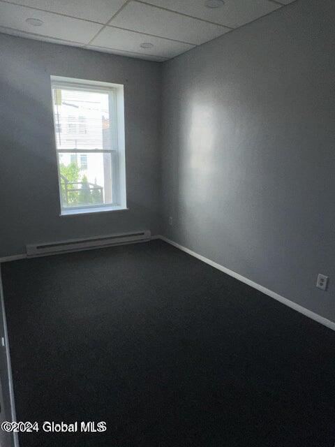 carpeted spare room featuring a baseboard radiator and a drop ceiling