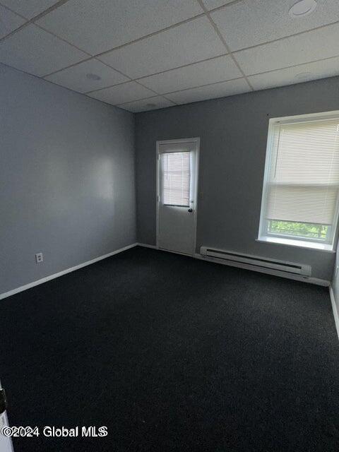 spare room with dark colored carpet, a drop ceiling, and a baseboard radiator