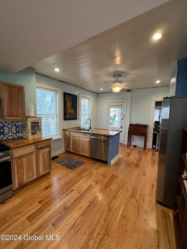 kitchen with kitchen peninsula, stainless steel appliances, ceiling fan, sink, and light hardwood / wood-style floors