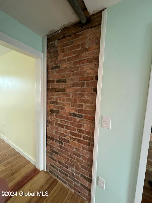 hallway with wood-type flooring and brick wall