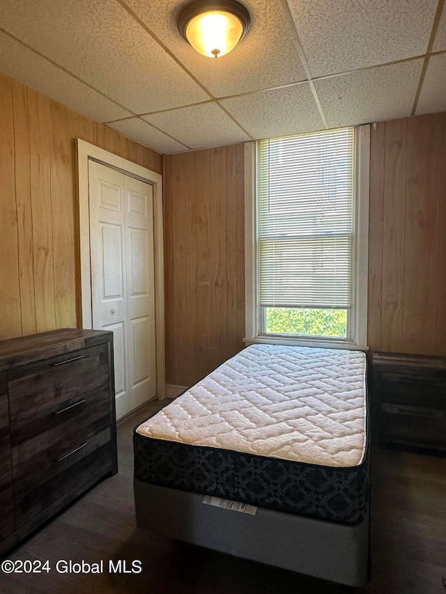 bedroom featuring a paneled ceiling, dark hardwood / wood-style floors, a closet, and wooden walls