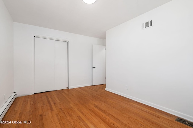 unfurnished bedroom featuring a closet, light hardwood / wood-style flooring, and a baseboard radiator