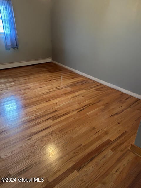 spare room with a baseboard radiator, baseboards, and wood finished floors