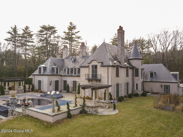 rear view of property featuring a lawn, a balcony, a patio, and a covered pool