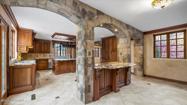 kitchen with crown molding, light stone counters, a center island, and a healthy amount of sunlight